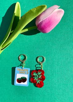 two key chains with tomatoes on them next to a pink tulip and green background