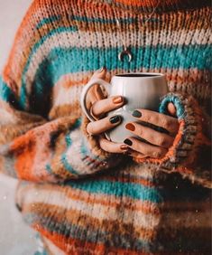 a woman holding a coffee cup with her hands wrapped around the mug while wearing striped sweater