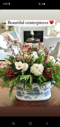 a vase filled with flowers and greenery on top of a wooden table in front of a fire place