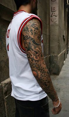 a man with a tattoo on his arm standing next to a building and looking down at the street