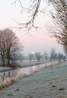 the sun is setting on a cold day over a small river and some bare trees