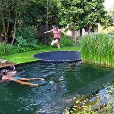 a person jumping into a pond with a trampoline in the water and some grass