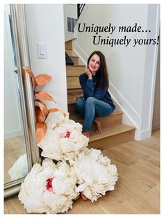 a woman is sitting on the stairs next to some white peonies in front of a mirror