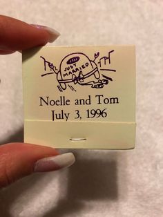 a person holding up a small stamp with the name noelle and tom on it