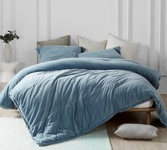 a bed with blue comforter and pillows on it in a white room next to a plant