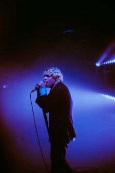 a man standing in front of a microphone on top of a blue stage with lights behind him