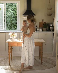 a woman holding a baby standing in front of a table