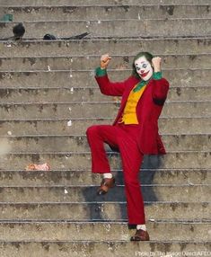 a man dressed as the joker is sitting on some steps and waving to someone with his hand up