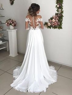 a woman standing in front of a wall wearing a white dress with flowers on it