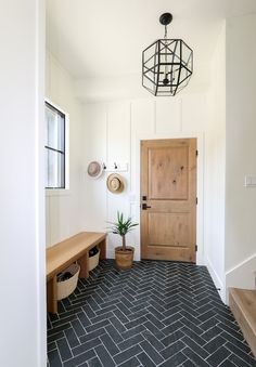 an entryway with a wooden door and black tile flooring next to a plant