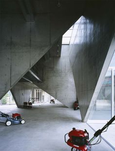 a red lawn mower sitting in the middle of a large room with concrete walls