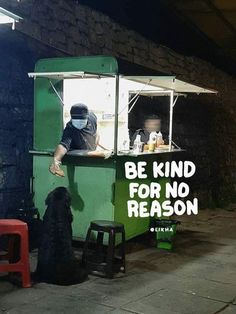 a man standing behind a green food cart with a dog sitting in front of it