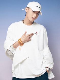 a young man wearing a white hat and holding his hand up to the side while standing in front of a blue wall