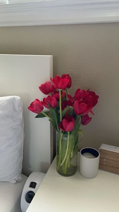 a vase filled with red flowers sitting on top of a white table next to a bed