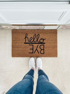 a person standing in front of a door mat that says hello bae