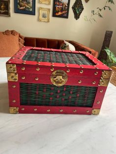 a red and black trunk sitting on top of a white table next to pictures hanging on the wall