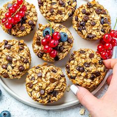 a person is picking up some granola on a plate with blueberries and cherries