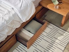 an open drawer on the side of a bed next to a night stand and nightstand