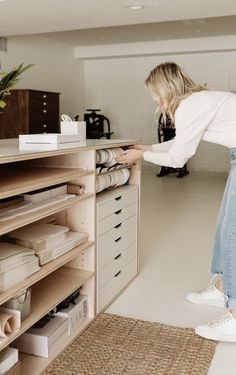 a woman standing in front of a shelf filled with boxes and papers on top of it