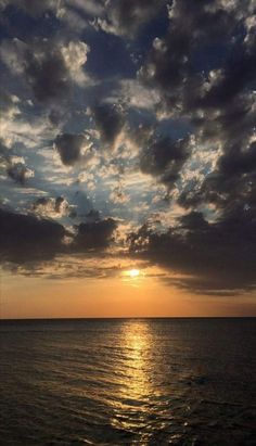 the sun is setting over the ocean with clouds in the sky and water below it