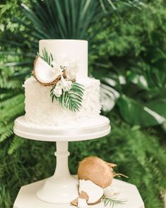 a white wedding cake with coconuts and flowers on the top is surrounded by greenery