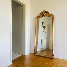 a large mirror sitting on top of a hard wood floor next to a white wall