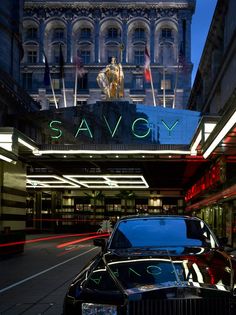 a black car is parked in front of the savovgy theatre sign at night