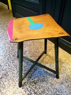 a small wooden table with an odd shape painted on it's top, sitting in front of a black door