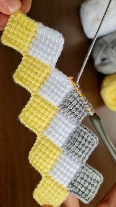 someone is using a pair of scissors to sew on some knitted material with yellow and white squares