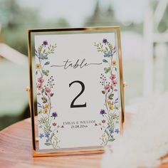 a wedding table number with flowers and leaves on it sitting on top of a wooden table