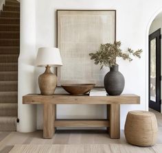 a table with two vases on it next to a lamp and some stairs in the background