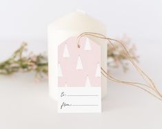 a candle with a tag on it sitting next to some pink flowers and greenery