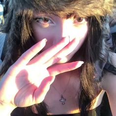 a woman wearing a fur hat covering her face with her hands and making a hand gesture