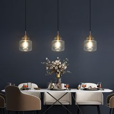 a dining room table with four hanging lights above it and flowers in vases on the table