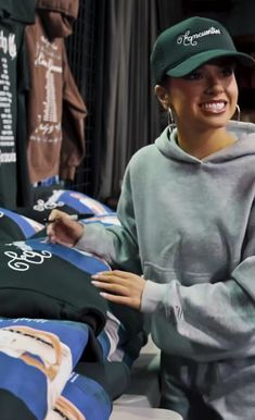 a woman is smiling and holding onto some shirts on display at a clothing store while wearing a green hat