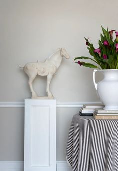 a white vase filled with flowers on top of a table next to a horse statue