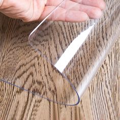 a person is holding a piece of clear plastic on a wooden surface with their hand