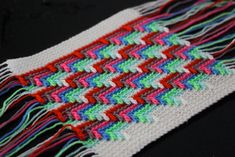 a close up of a multicolored scarf on a black surface with fringes