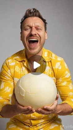 a man in yellow shirt holding a large white ball with his mouth open and tongue out