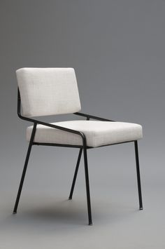 a white chair with black legs and a seat cushion on the back, in front of a gray background