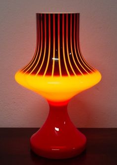 a red and yellow lamp sitting on top of a table next to a white wall