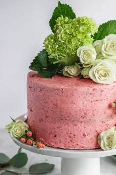 a pink cake with white flowers and greenery on top is sitting on a pedestal