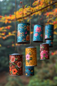 colorful tin canisters hanging from a tree branch with flowers painted on the sides