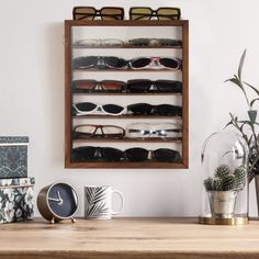 a wooden shelf filled with lots of sunglasses on top of a table next to a clock