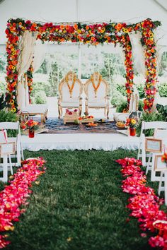 an outdoor ceremony setup with white chairs and red flowers on the grass under a tent