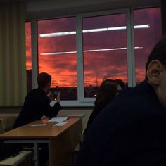 two people sitting at desks in front of a window with the sun setting behind them