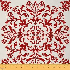 a red and white fabric with an intricate design on it's back side, next to a ruler