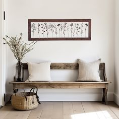 a wooden bench sitting in front of a white wall with flowers and plants on it