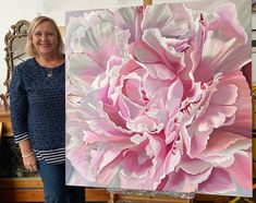 a woman standing next to a large pink flower on a easel in front of a painting