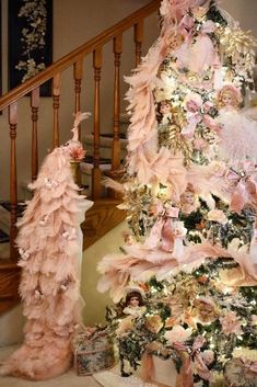 a pink christmas tree decorated with feathers and other decorations on top of a stair case